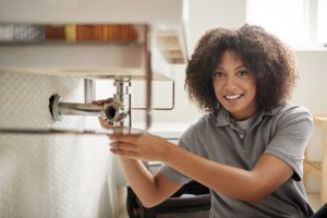 female plumber sitting on the floor fixing a bathroom sink