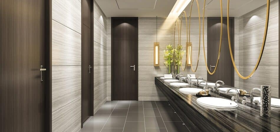 Modern public restroom featuring dark wood stalls, large mirrors with gold frames, multiple sinks, and decorative lighting—showcasing a recent hotel plumbing upgrade for enhanced comfort and style.