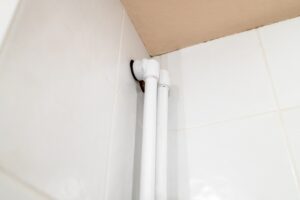 Several white PVC vent pipes in bathroom plumbing, secured with metal brackets, are mounted on a plain, unfinished concrete wall, creating a network of angles and connections.