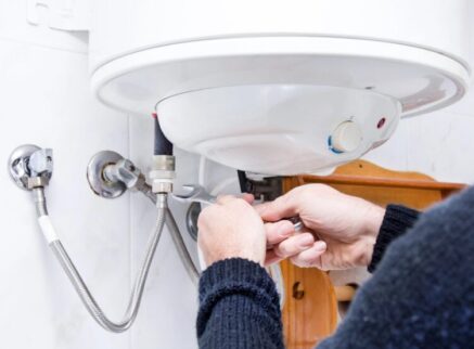 A person uses a wrench to adjust plumbing connections under a wall-mounted water heater