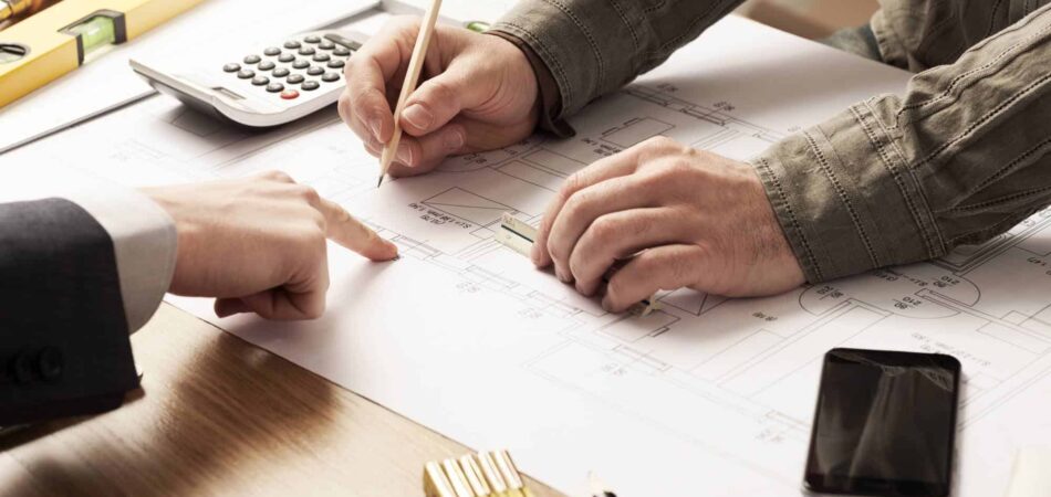 Two people are collaborating on a blueprint, using a calculator and pencil to plan their project