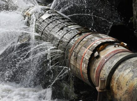 Water flows out of a pipe, creating a small stream on the ground below.