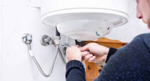 A person uses a wrench to adjust plumbing connections under a wall-mounted water heater