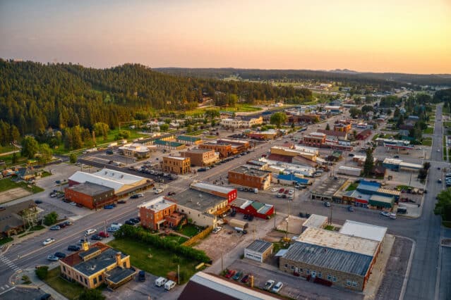 Aerial view of a small town with low-rise buildings, tree-lined streets, and surrounding greenery at sunset.