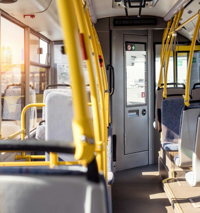 Interior of a city bus with empty blue and gray seats, yellow handrails, and sunlight streaming through the windows.