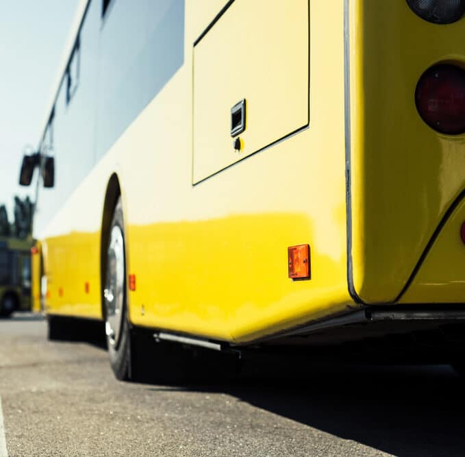 Close-up view of a yellow city bus parked on a paved lot, with another bus visible in the background.
