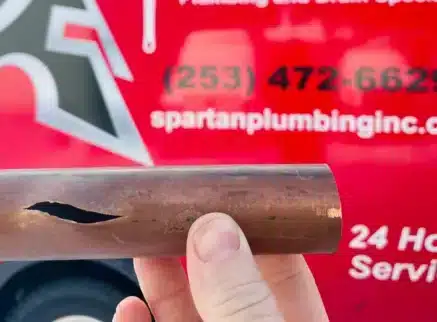 Split copper pipe held up in front of a Spartan Plumbing service truck