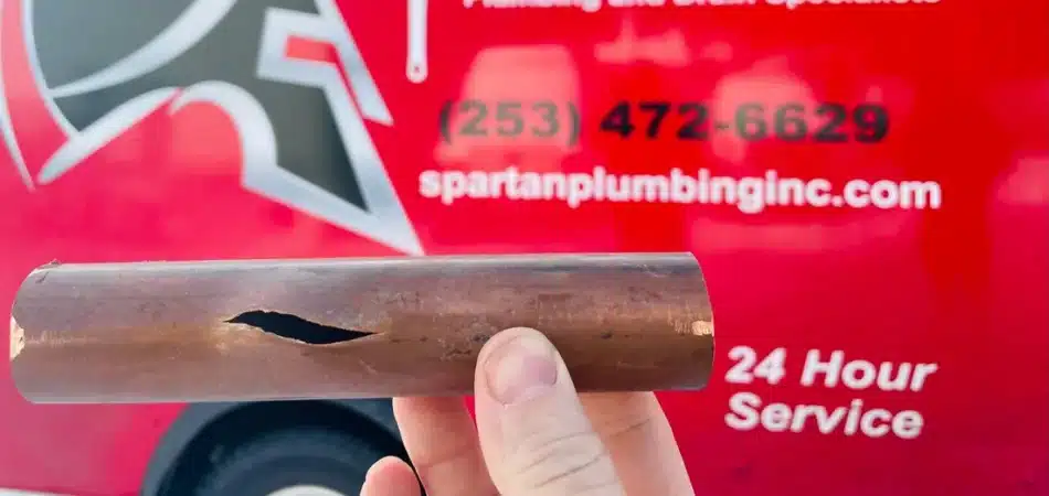 Split copper pipe held up in front of a Spartan Plumbing service truck