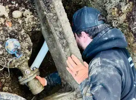 Spartan Plumbing technician working on a water main line and valve in an excavated pit